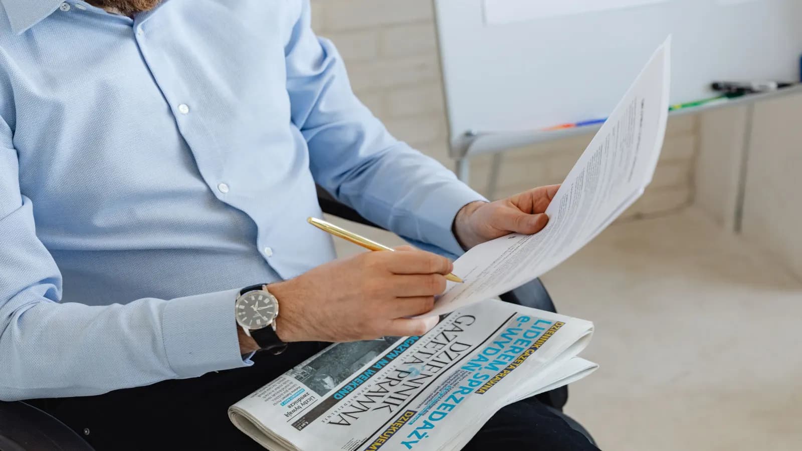 Person prüft ein ausgedrucktes Manuskript mit Stift, daneben eine Tageszeitung — Symbolbild für redaktionell geprüfte Texte von öffentlichem Interesse